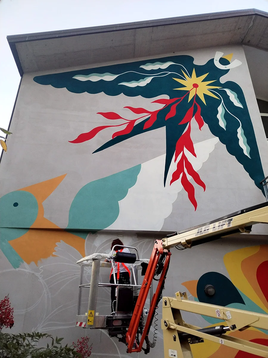 Veduta della sezione superiore del murale di Rosmunda a Rovigo: un sole stilizzato nero e oro circondato da forme sinuose bianche, rosse e teal che richiamano piumaggi o elementi vegetali astratti.