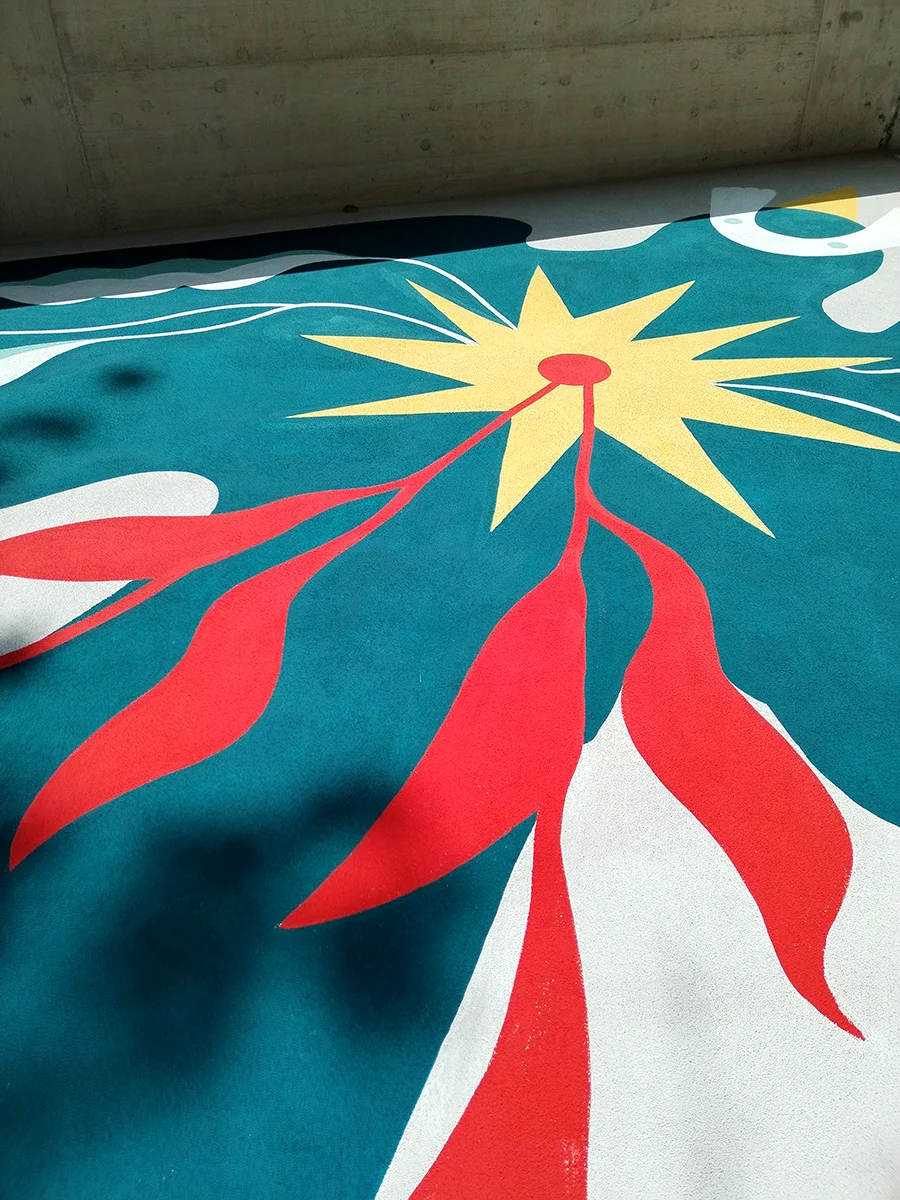 Primo piano del sole stilizzato nel murale di Rovigo: focus sulla precisione delle linee e sul contrasto cromatico tra il giallo centrale, il rosso dei raggi e il blu profondo dello sfondo.