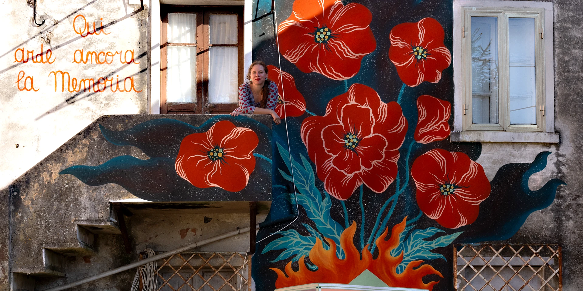 Dettaglio della foto dell'artista Rosmunda affacciata al balcone del secondo piano dove ha esiguito l'opera Qui Arde ancora la Memoria a Bergiola, Carrara.