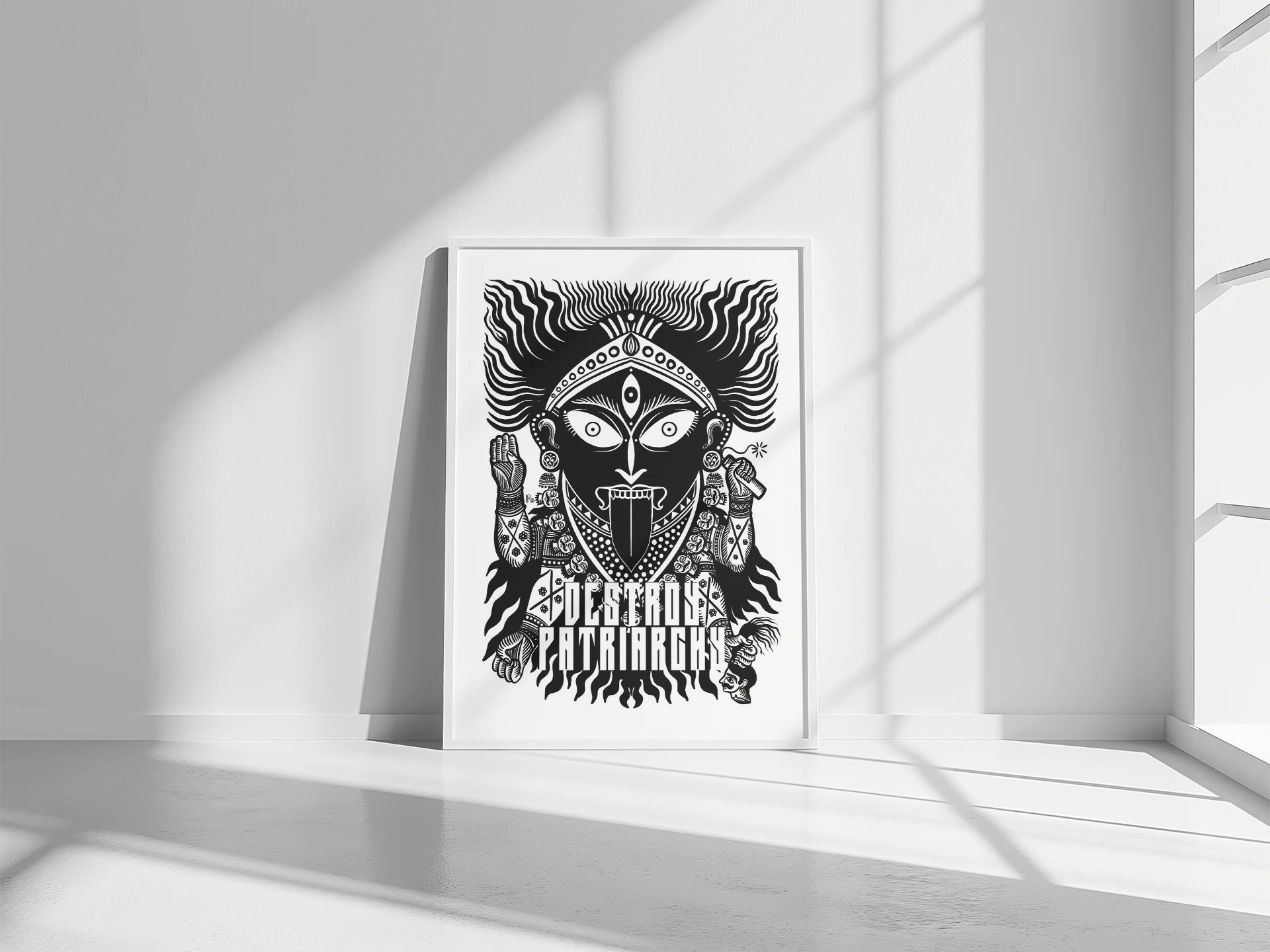 Mockup dell'opera "Destroy Patriarchy" di Rosmunda incorniciata in nero e appoggiata su un pavimento in legno chiaro contro una parete bianca. L'illustrazione mostra la Dea Kali in bianco e nero, simbolo della distruzione delle strutture oppressive.