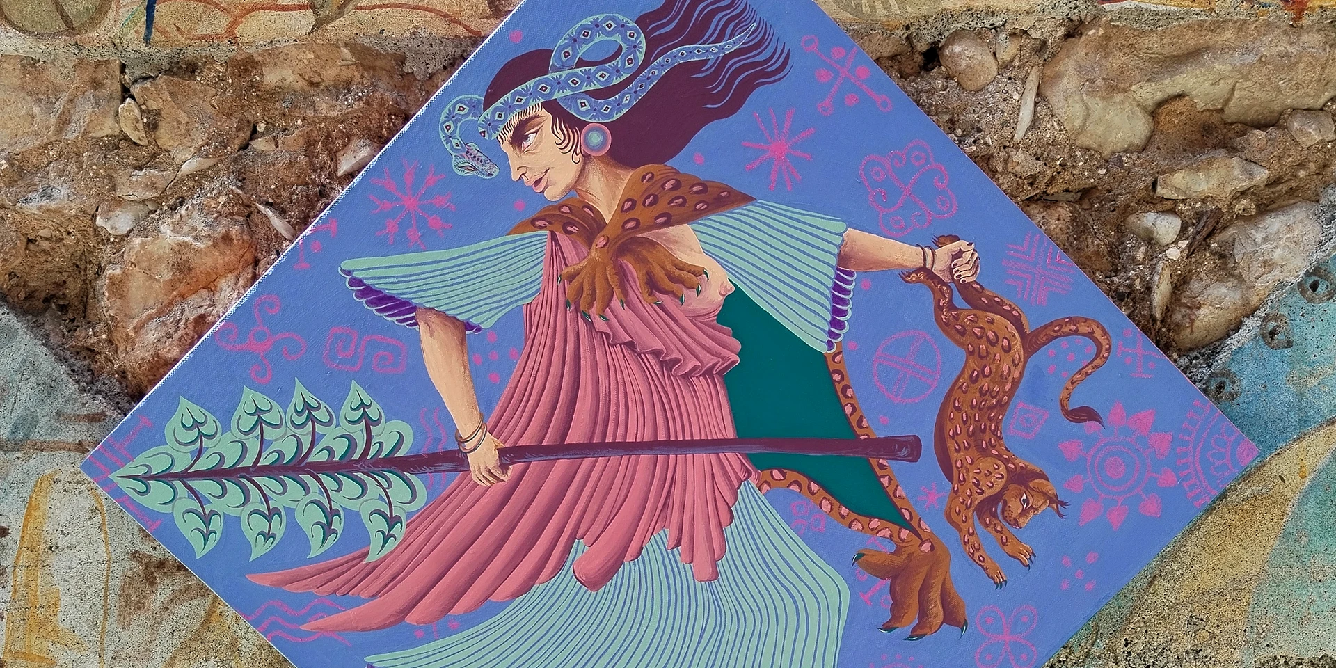 Primo piano dell'opera "Ekstasis" di Rosmunda che mostra una figura mitologica femminile in vesti classiche rosa e azzurre, mentre tiene un bastone rituale e conduce un ghepardo. L'opera, ricca di simboli e decorazioni a contrasto, è realizzata su una superficie romboidale blu integrata in una parete con texture naturale e motivi organici.