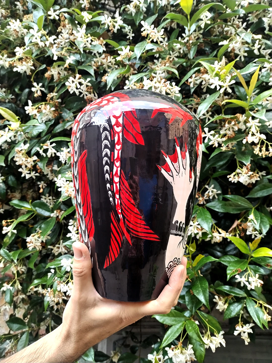 La mano palamta con le unghie rosse della Sirena arriva quasi a toccare la pinna della sua stessa coda. Il vaso smaltato riflette l'artista nell'atto di fare questa foto.
