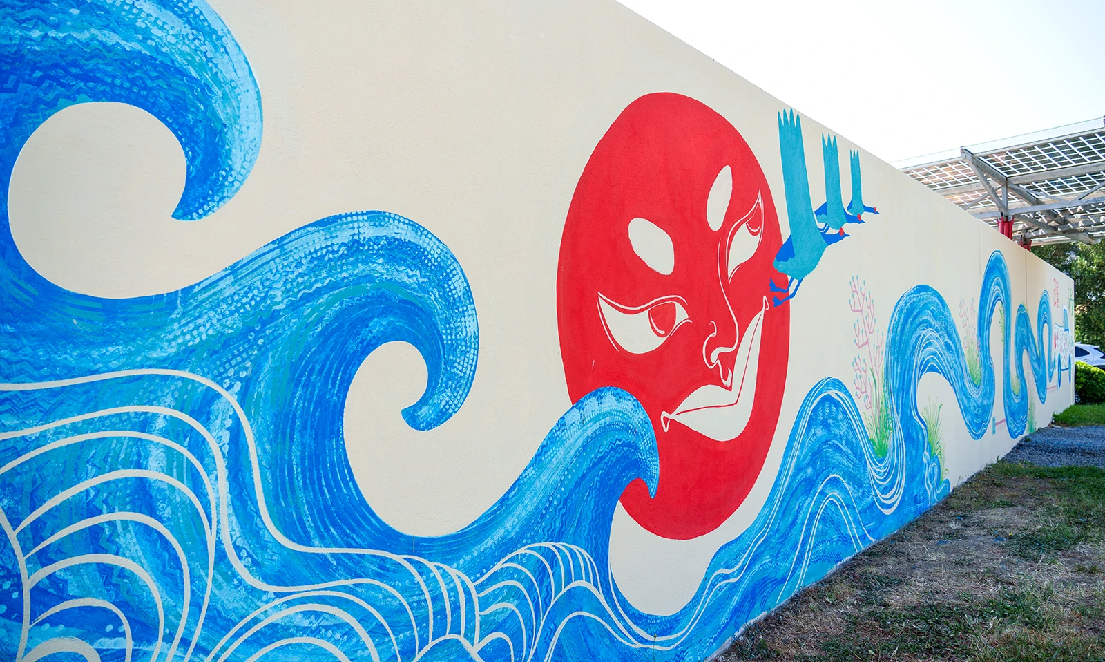 Veduta prospettica del murale per Toyota: il grande sole rosso centrale è circondato da onde blu dinamiche e gru in volo, con la parete che si estende verso il parcheggio esterno.