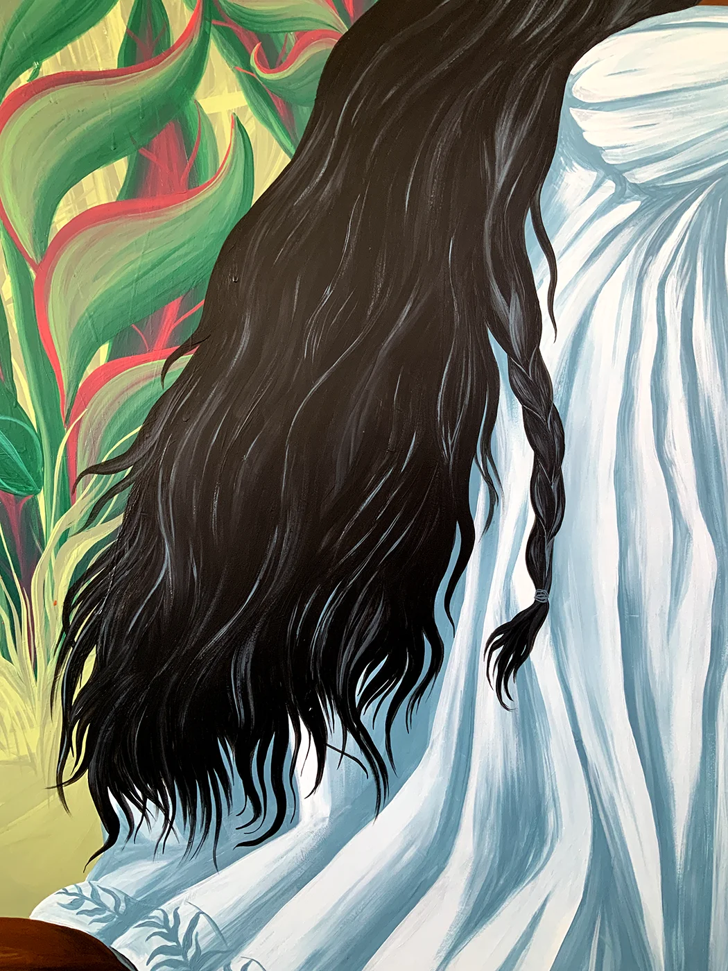 Dettaglio verticale del murale Embrace Your Fears di Rosmunda che mostra la schiena e i lunghi capelli neri intrecciati della bambina, vestita con una tunica bianca a pieghe, mentre si staglia contro una fitta vegetazione tropicale.