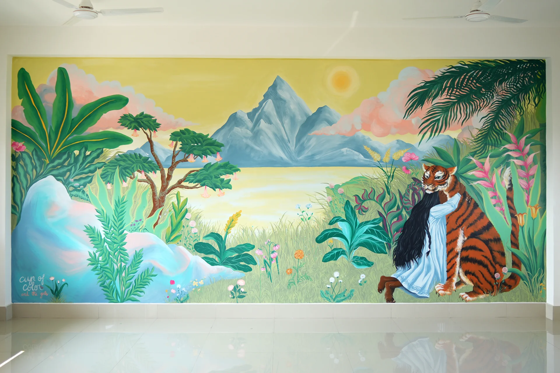 Veduta d'insieme dell'opera Embrace Your Fears di Rosmunda all'interno di un'aula scolastica in India, che mostra l'intero murale con una bambina che abbraccia una tigre circondata da una giungla rigogliosa, montagne blu e un cielo dorato con il sole.
