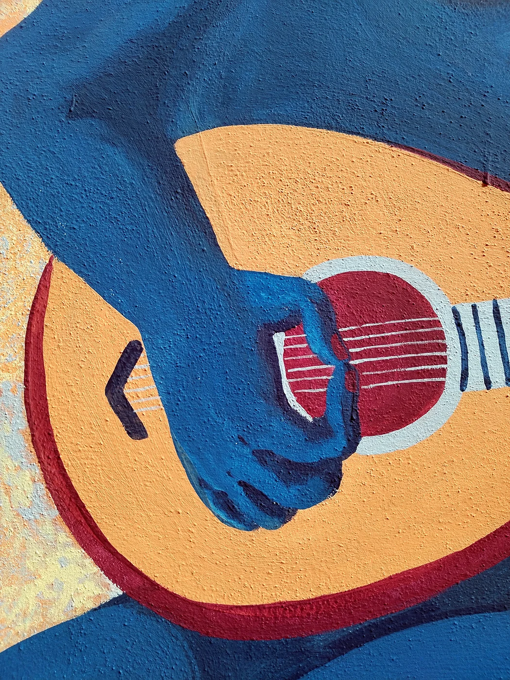 Dettaglio del murale "Il Segreto di Villa Chioso" che mostra un primo piano ravvicinato di una mano blu intenta a pizzicare le corde di uno strumento musicale simile a un liuto o a una chitarra stilizzata, dipinto con una texture materica su uno sfondo ocra e rosso.