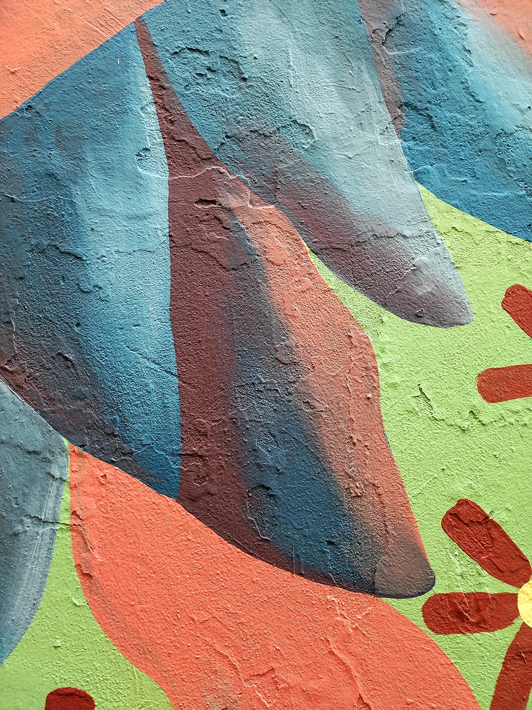 Dettaglio del murale 'Piccione Viaggiatore' di Rosmunda che mostra le piume colorate dell'uccello nei toni del blu, grigio e rosso, con una porzione di sfondo verde menta e un fiore stilizzato sulla destra.