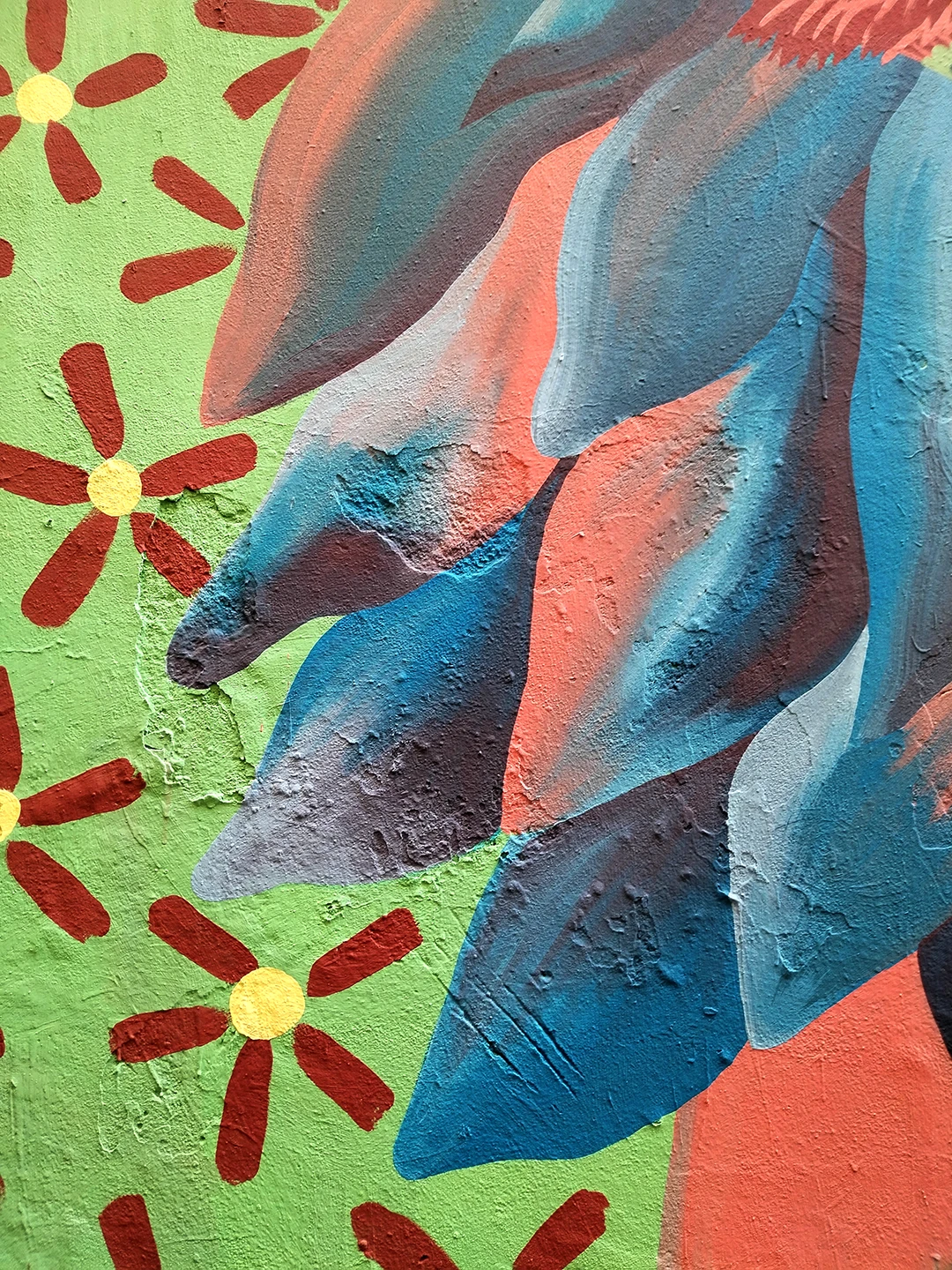 Dettaglio verticale del murale 'Piccione Viaggiatore' di Rosmunda che mostra un insieme di piume stilizzate nei toni del blu, azzurro e grigio su uno sfondo verde menta decorato con piccoli fiori rossi e gialli.