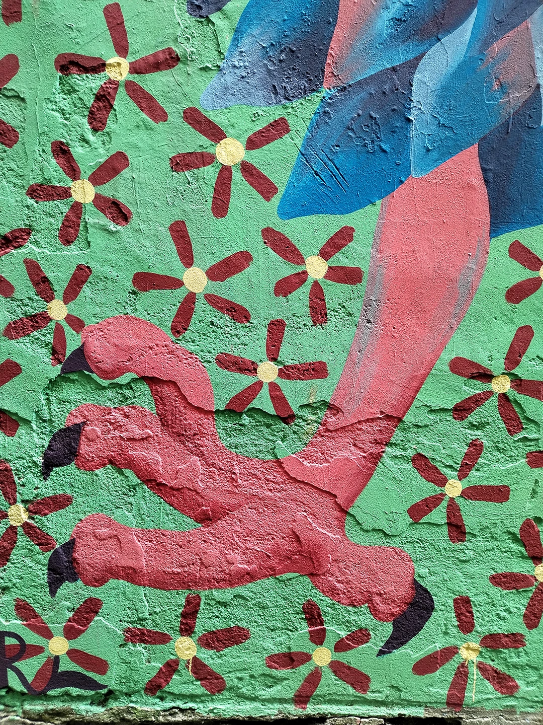 Dettaglio verticale del murale Piccione Viaggiatore di Rosmunda focalizzato sulla zampa dell'uccello antropomorfo, dipinta con sfumature di rosso e rosa, immersa in un campo di piccoli fiori stilizzati su sfondo verde.