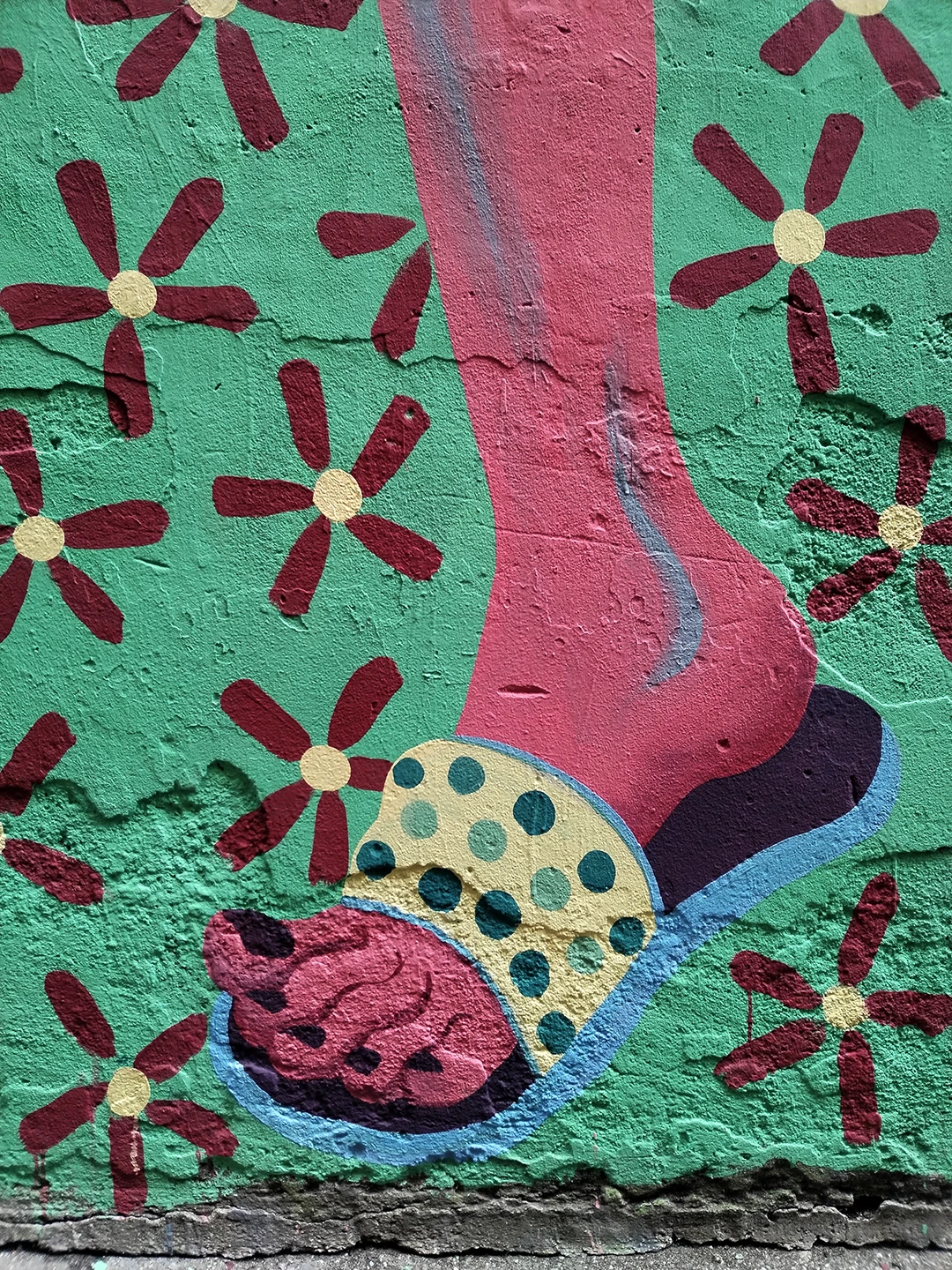 Dettaglio verticale del murale Piccione Viaggiatore di Rosmunda focalizzato sulla zampa inferiore dell'uccello antropomorfo, dipinta nei toni del rosa e del bordeaux, che indossa un sandalo azzurro a pois gialli su uno sfondo verde menta decorato con fiori stilizzati.