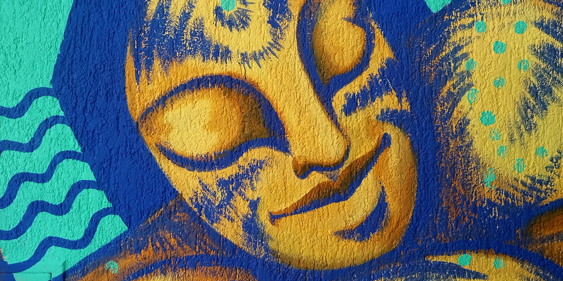 Veduta d'insieme del murale 'Sphinx' di Rosmunda: una monumentale figura mitologica distesa che occupa l'intera parete esterna, con il volto dorato e il corpo decorato da pattern gialli e blu che contrastano con lo sfondo rosa acceso dell'edificio.
