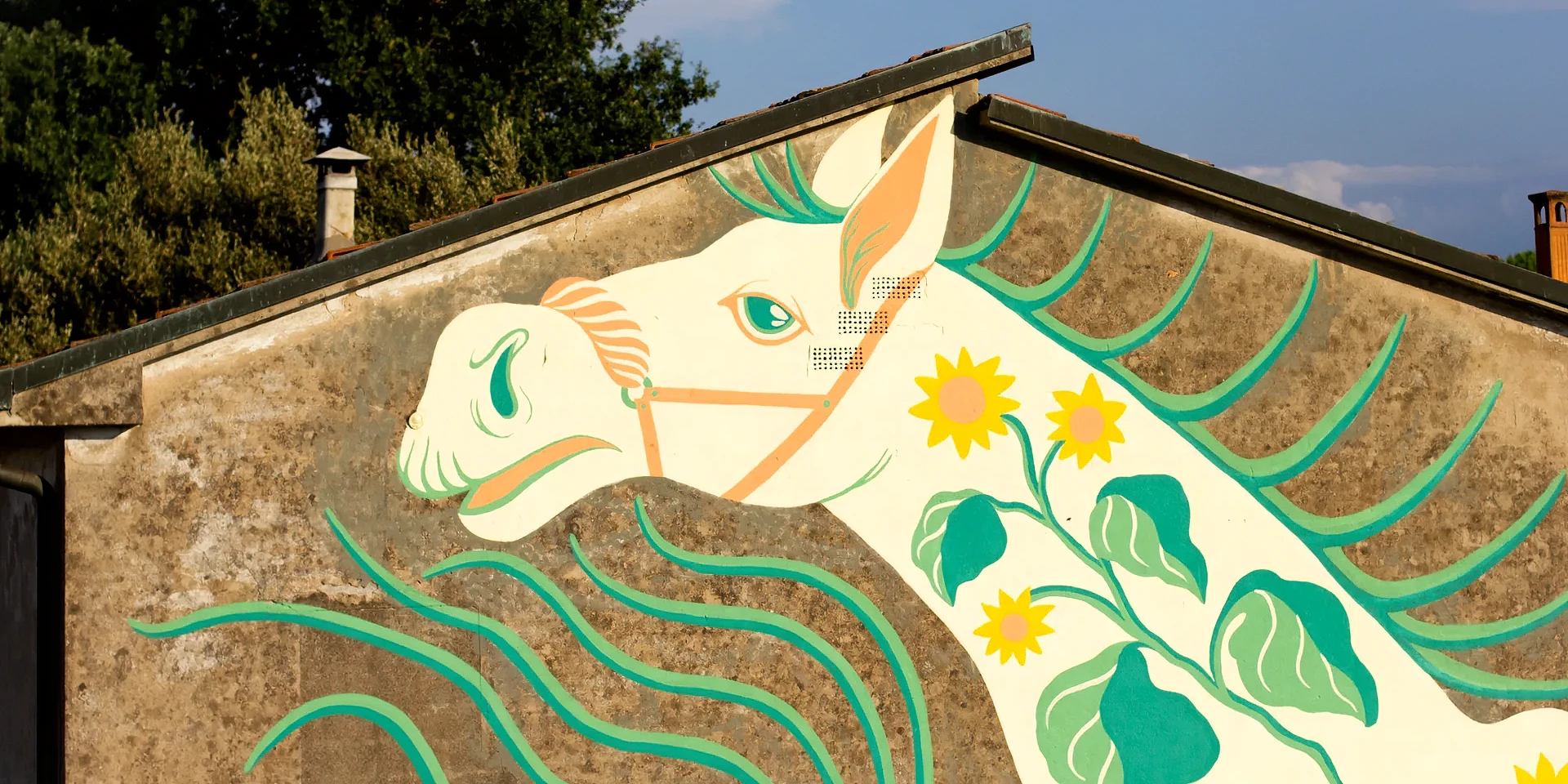 Dettaglio del murale "Tormento, Cavallo Contento" di Rosmunda che raffigura la testa stilizzata di un cavallo bianco con finimenti arancioni, decorata sul collo con grandi fiori gialli e foglie verdi, su uno sfondo murario con onde color acquamarina.