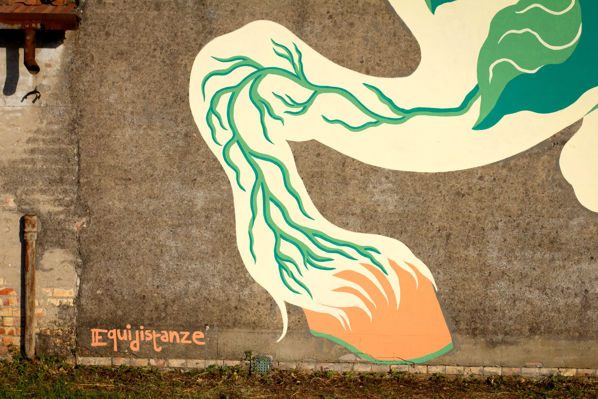 Dettaglio del murale "Tormento, Cavallo Contento" di Rosmunda che raffigura la parte inferiore di un cavallo stilizzato con una zampa arancione e verde, accanto alla scritta "Equidistanze" tracciata sulla base di un muro rurale.